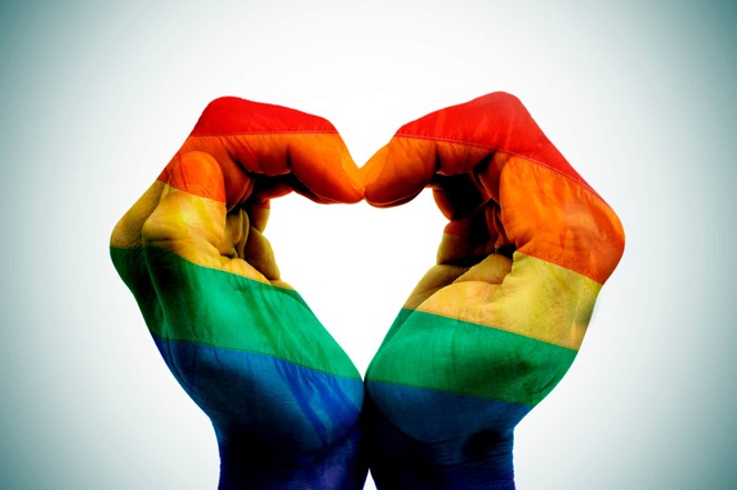 Photo of a heart made with hands and painted with the rainbow flag
