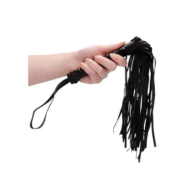 a hand holding a black flogger with a patterned handle and a black wrist strap
