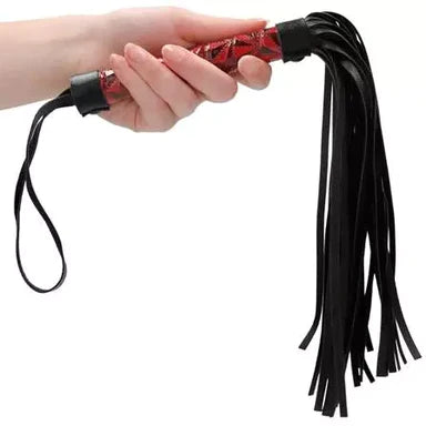 a hand holding a black flogger with a red patterned handle and a black wrist strap