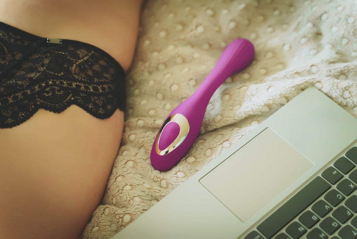 Photo of a vibrator between a woman and a laptop on a bed