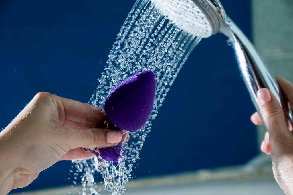Photo of a person holding a silicon anal plug under a shower head