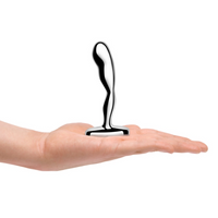 Metallic anal plug held in a hand on a white background