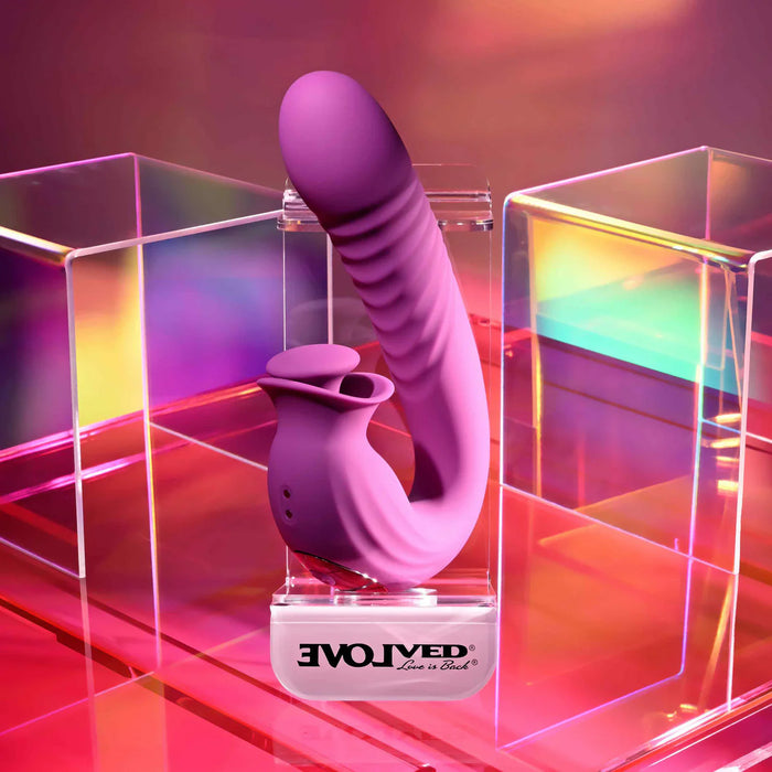 Purple vibrator with clit thumper with 'EvolvEd' branding on a reflective surface