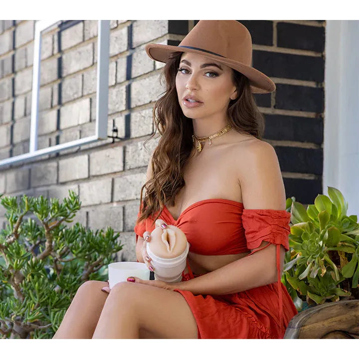 abigail mac sitting on bench outside with hat and red dress holding a fleshlight