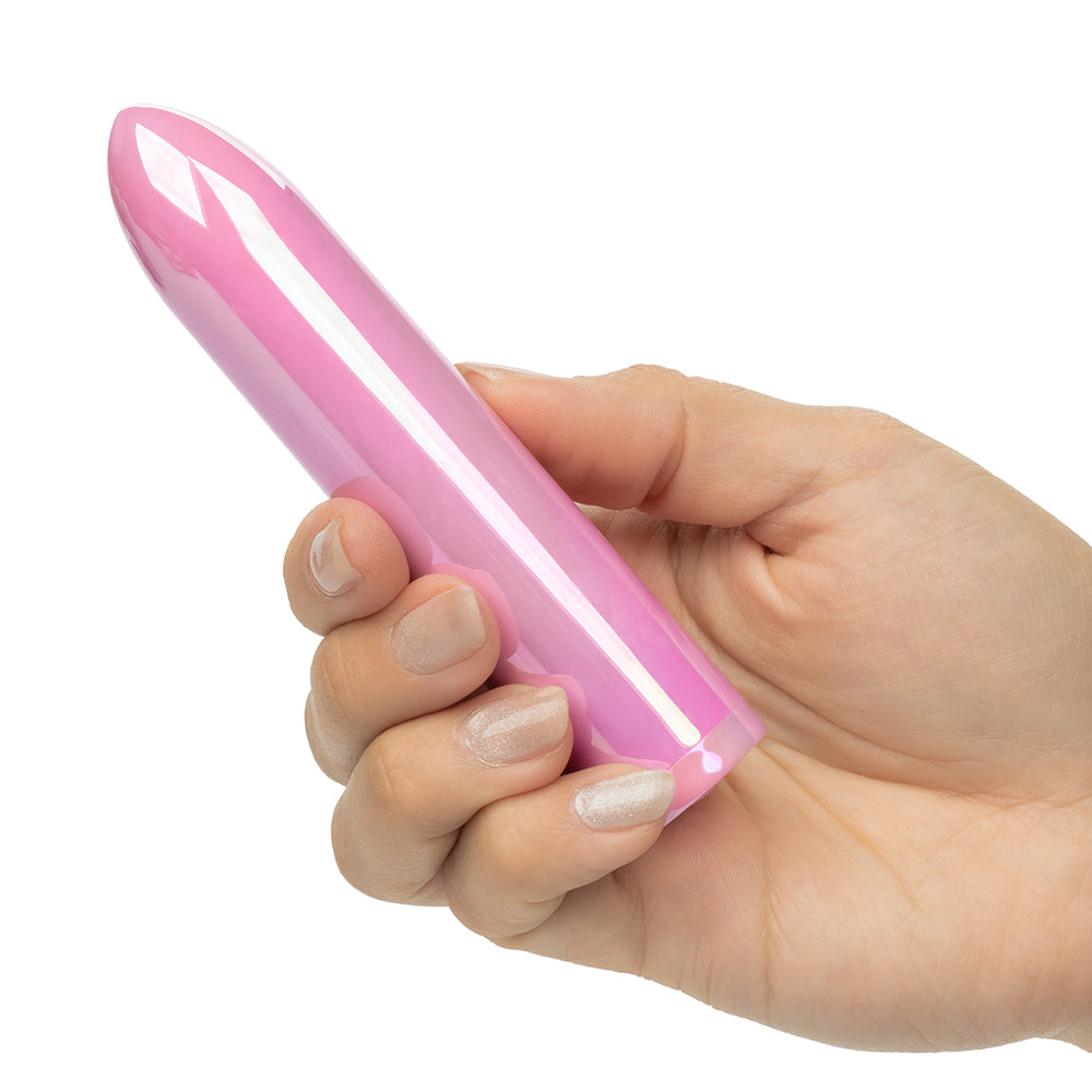 A hand with light pink glitter nail polish holding a glossy, pink, bullet-shaped personal massager against a solid white background.