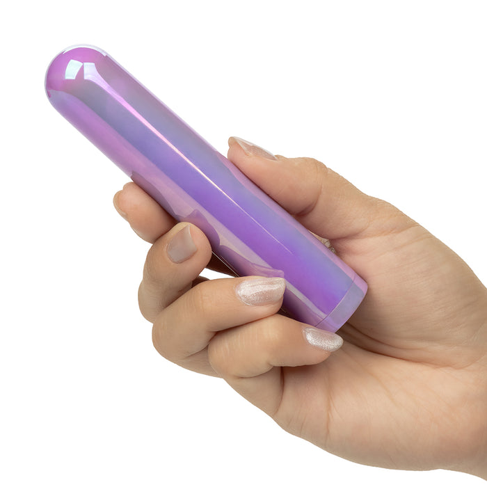 A hand holding a glossy, iridescent purple vibrator against a solid white background.