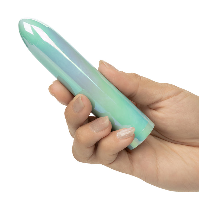 A hand holding a smooth, glossy, bullet-shaped object with a mint green and light blue iridescent finish, set against a plain white background.