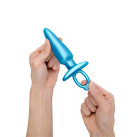 Blue anal plug held by two hands against a white background