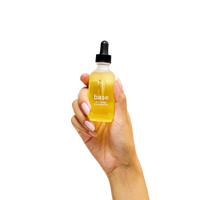 Hand holding a bottle labeled 'base' with a dropper on a white background