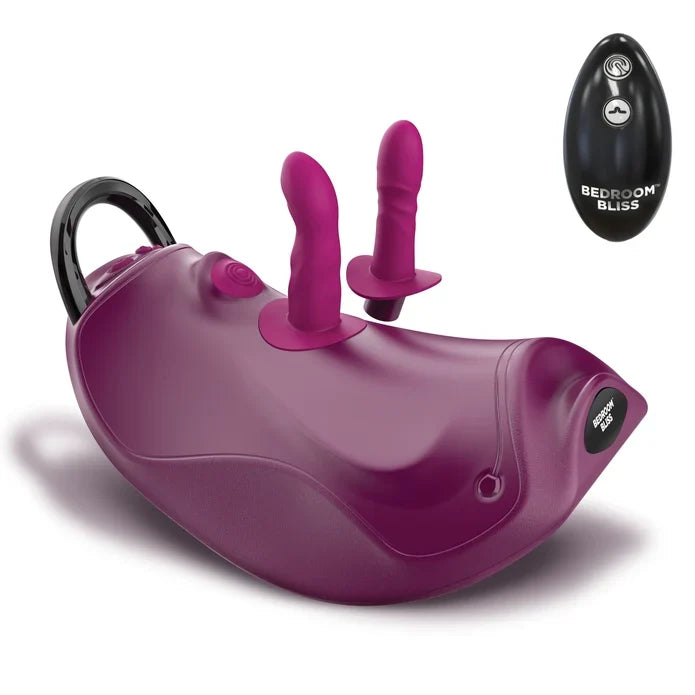 A purple and magenta dual-stimulation personal massager with a black carrying handle, shown alongside its black wireless remote control labeled 'BEDROOM BLISS'.