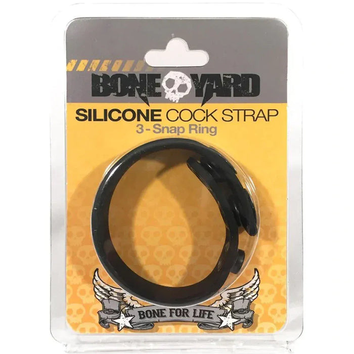 A black silicone cock strap with a 3-snap ring, packaged in a clear blister pack with a yellow and gray Bone Yard brand card.