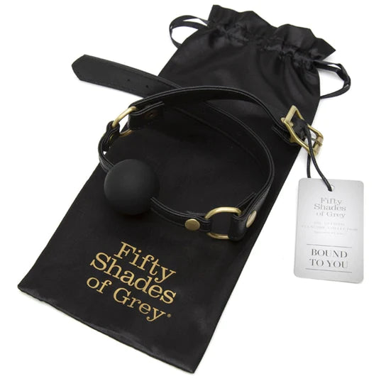 a black ball gag with black straps and golden accents. It is sitting on a black storage bag with golden letters