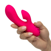 A hand holding a bright pink silicone personal massager with a curved shaft and dual bulb ends, shown against a plain white background.