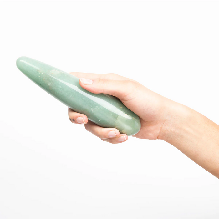 Hand holding a green stone dildo against a white background