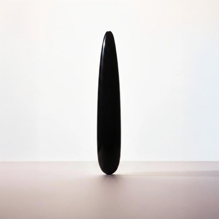 A single black teardrop-shaped stone or ceramic object stands upright on a plain light surface against a white background.