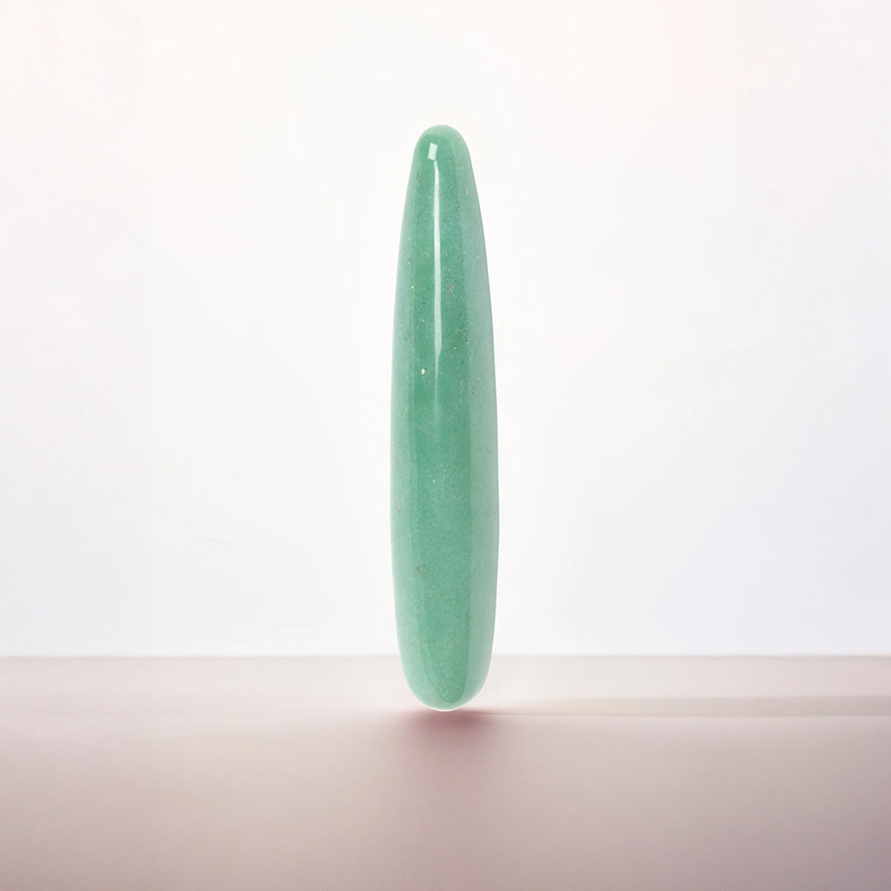 A polished light green jadeite cylindrical wand or crystal pointer standing upright on a neutral surface against a clean white background.
