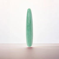 A polished light green jadeite cylindrical wand or crystal pointer standing upright on a neutral surface against a clean white background.