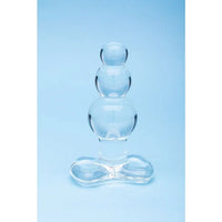 A clear glass balloon-style adult novelty product with three stacked spherical chambers and a wide base, photographed against a light blue studio background.