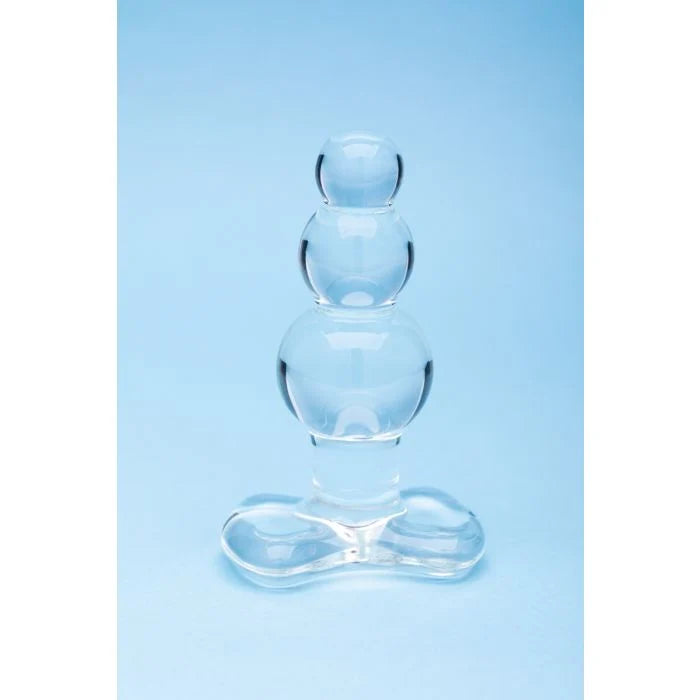 A clear glass balloon-style adult novelty product with three stacked spherical chambers and a wide base, photographed against a light blue studio background.
