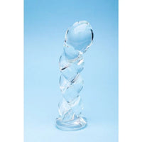 A clear glass spiral dildo standing upright on a light blue background.