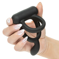 Black closer caress cock ring held in a hand with white nail polish on a white background