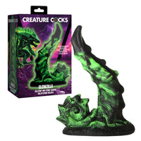Glowing green silicone dildo with packaging labeled 'Creature Cocks' on a white background