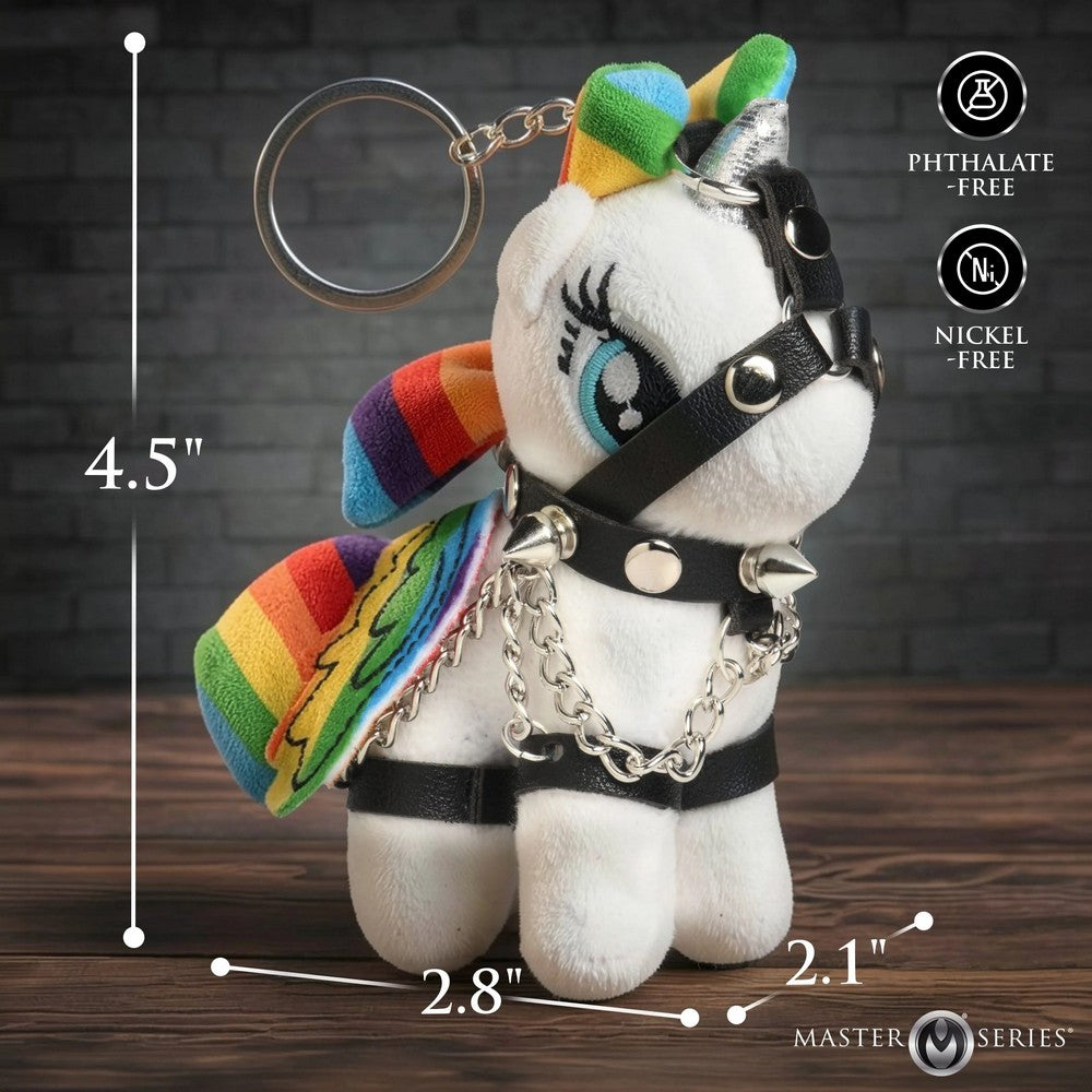 A white plush unicorn keychain with rainbow accents, black leather-style harness details, and silver chains, shown on a wooden surface against a dark brick background. Measurement lines indicate dimensions of 4.