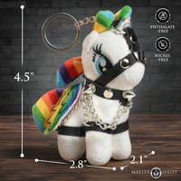 A white plush unicorn keychain with rainbow accents, black leather-style harness details, and silver chains, shown on a wooden surface against a dark brick background. Measurement lines indicate dimensions of 4.
