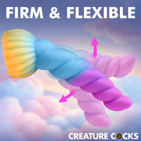 A 3D-rendered twisted novelty product with a yellow-to-blue-to-purple-to-pink gradient, shown against a pastel cloud background with the text 'FIRM & FLEXIBLE' and 'CREATURE COCKS'. Pink arrows indicate flexibility.