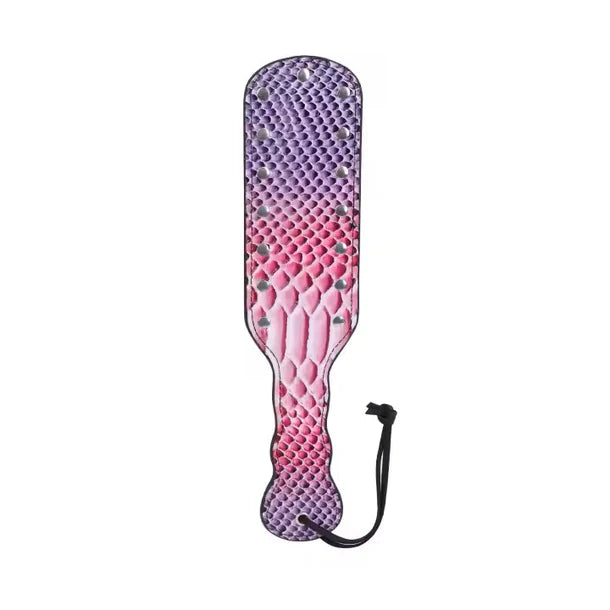 A paddle-style strap-on accessory with a textured reptile-skin pattern in a purple-to-pink gradient, featuring small metallic studs and a black wrist strap, shown on a plain white background.