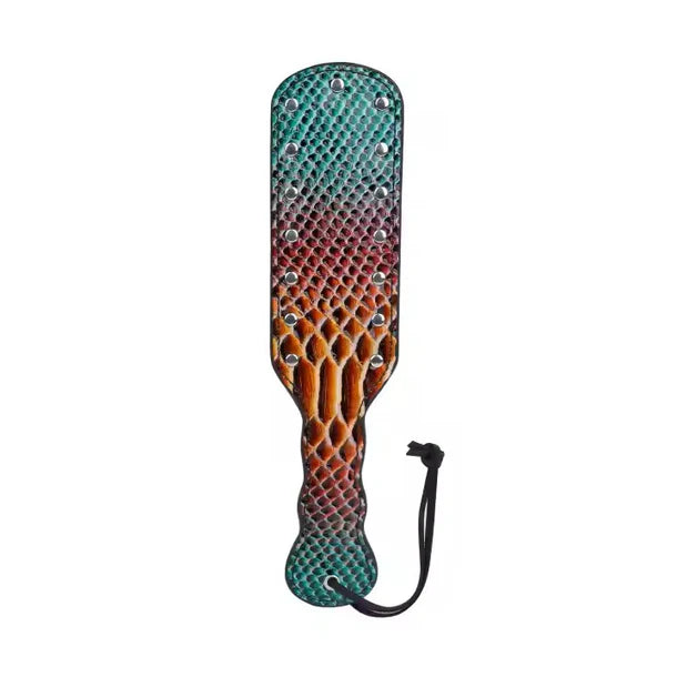 A paddle-style strap-on paddle with a textured reptile-skin pattern featuring a gradient of teal green, purple, orange, and brown, embellished with silver studs and a black wrist strap, shown on a plain white background.