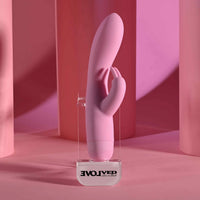 Pink silicone rabbit vibrator on a clear stand with 'Evolvied' branding against a pink background