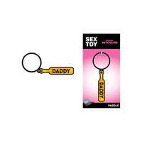The image features the "Daddy Paddle Keychain" by Woodrocket, a whimsical and playful accessory. The keychain is depicted in a vibrant yellow color with the word "DADDY" inscribed in bold, black letters, creatively designed to resemble a BDSM paddle.
