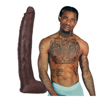 Man with tattoos holding a large brown molded dildo against a white background