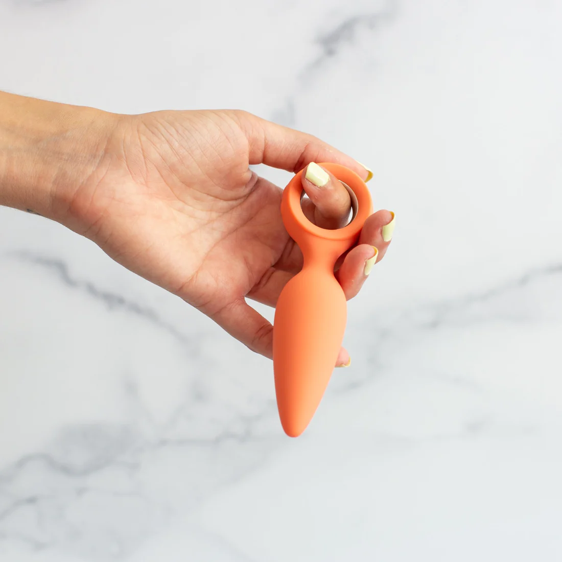 orange carrot butt plug held in hand by finger ring