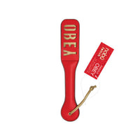 A red leather strap with gold lettering that reads 'Obey' and a red paper tag attached by a tan cord, shown on a plain white background.