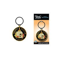 The image features a black and gold metal keychain with the phrase "Fresh Outta F***s" written in bold, stylized lettering, accompanied by a graphic of a skull. The keychain is displayed both attached to its packaging and separately to highlight the design and text.