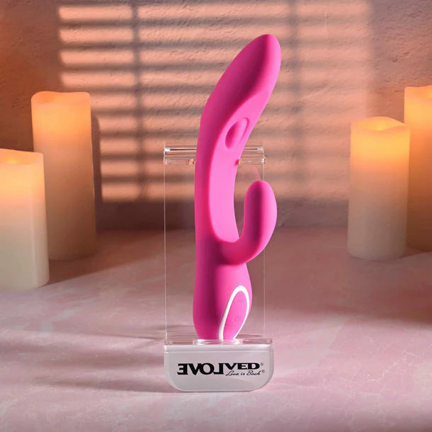 Pink silicone vibrator on a clear stand with candles in the background