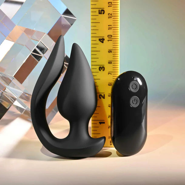 'The Genie' silicone vibrating anal plug with remote control next to a measuring tape on a reflective surface.