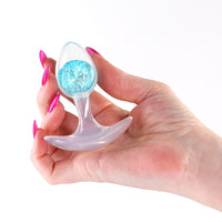 Hand holding a glams cosmic glass anal plug in blue on a white background