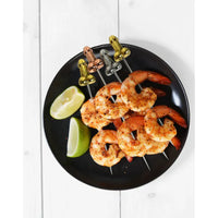 Skewers of grilled shrimp on a black plate with lime wedges.