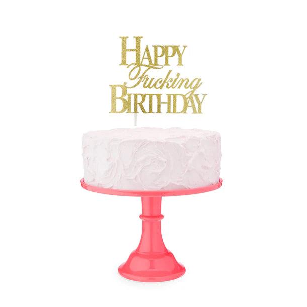 White cake with a pink stand and 'Happy Fucking Birthday' topper on a white background