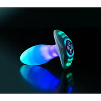 Glowing blue and green anal plug on a reflective surface with a black background