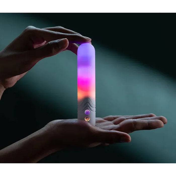 Hand holding a glowing illumination the bullet vibrator with multicolor light on a dark background