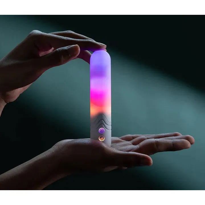 Hand holding a glowing illumination the bullet vibrator with multicolor light on a dark background