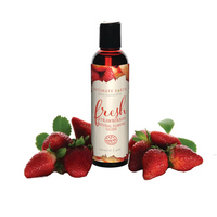 Bottle of Intimate Earth strawberry-flavored natural flavors glide with fresh strawberries on a white background