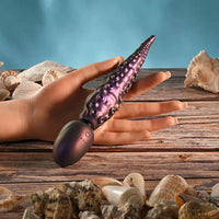 Hand holding a purple and black vibrator with seashells on a wooden surface