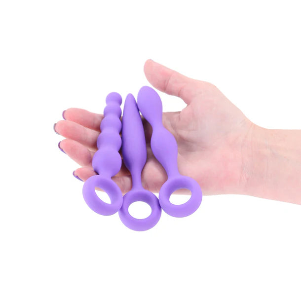 Purple silicone anal plugs held in a hand against a white background