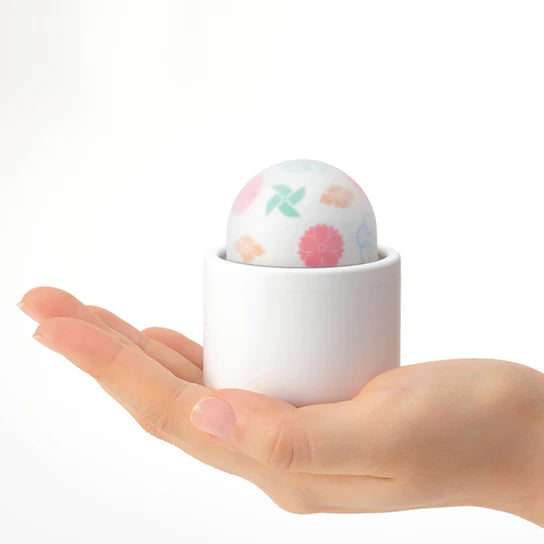 a hand holding a white cylindrical base with a color patterned vibrating ball top