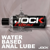 JOCK Extreme water-based anal lube bottle with a glass on a gray background